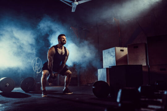 Circuit Workout muscular attractive caucasian bearded man lifting two kettlebells gym weight plates dumbbell tires background