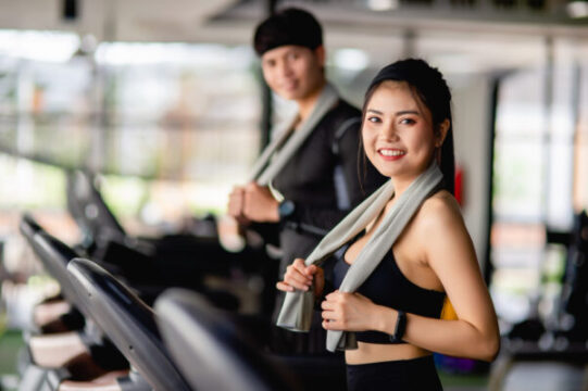 selective focus portrait sexy woman sportswear running treadmill blurred handsome man run nearly they are workout modern fitness gym smile copy space