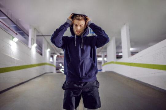 young sportsman putting hoodie head while standing underground garage