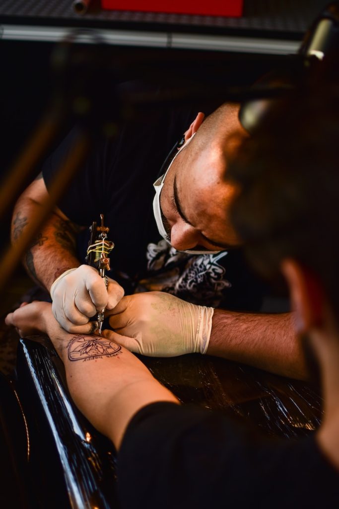 man doing tattoo on human arm Exploring the Motivation Behind Gym Logo Tattoos: Unveiling the Fascination