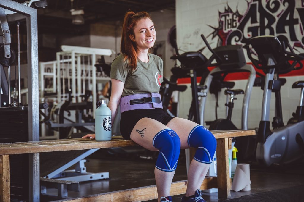 woman sitting on brown wooden bench at the gym How to Inception Powerlifting as a Woman
