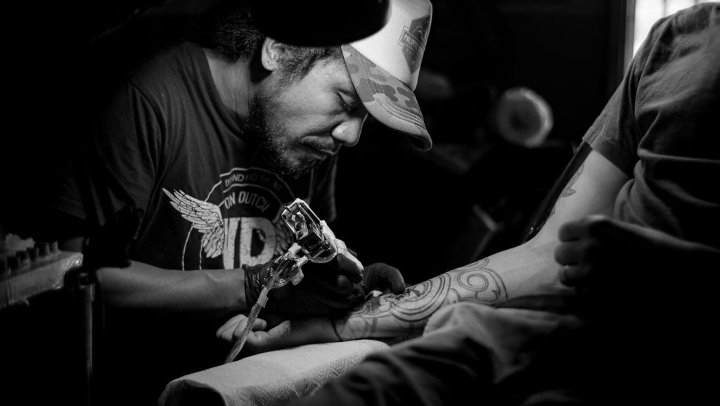 grayscale photo of man doing tattoo Exploring the Motivation Behind Gym Logo Tattoos: Unveiling the Fascination