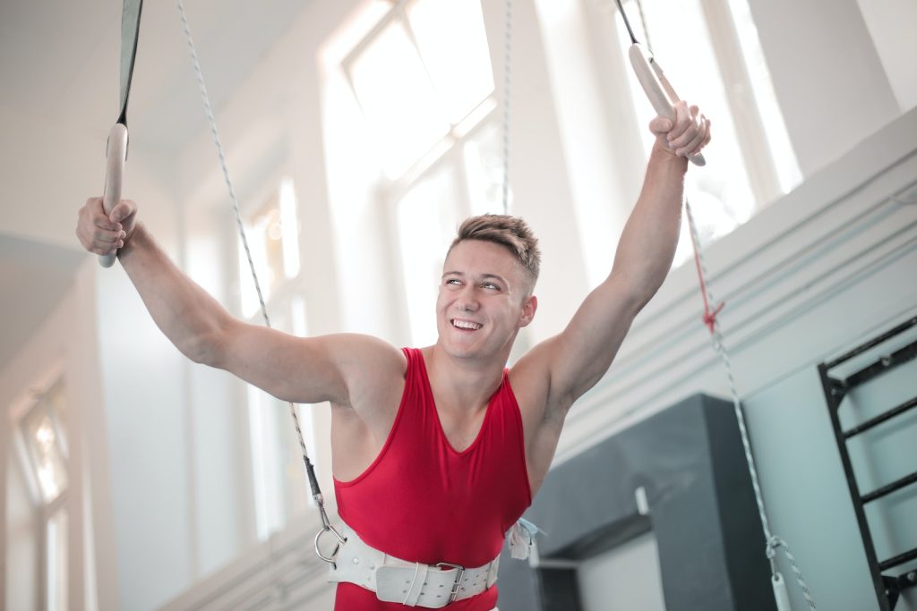 Ring Workout Powerful male gymnast in safety belt on waist holding rings while smiling and looking away before doing tricks