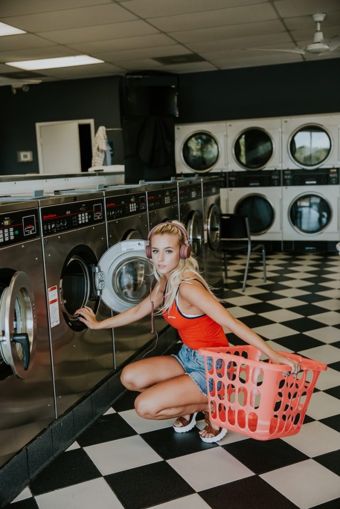 woman kneeling in front of front-load clothes washer inside laundry shop