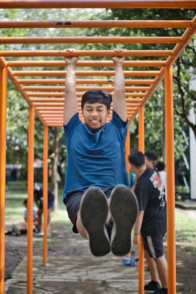 Pull-up man in blue crew neck t-shirt sitting on brown wooden swing