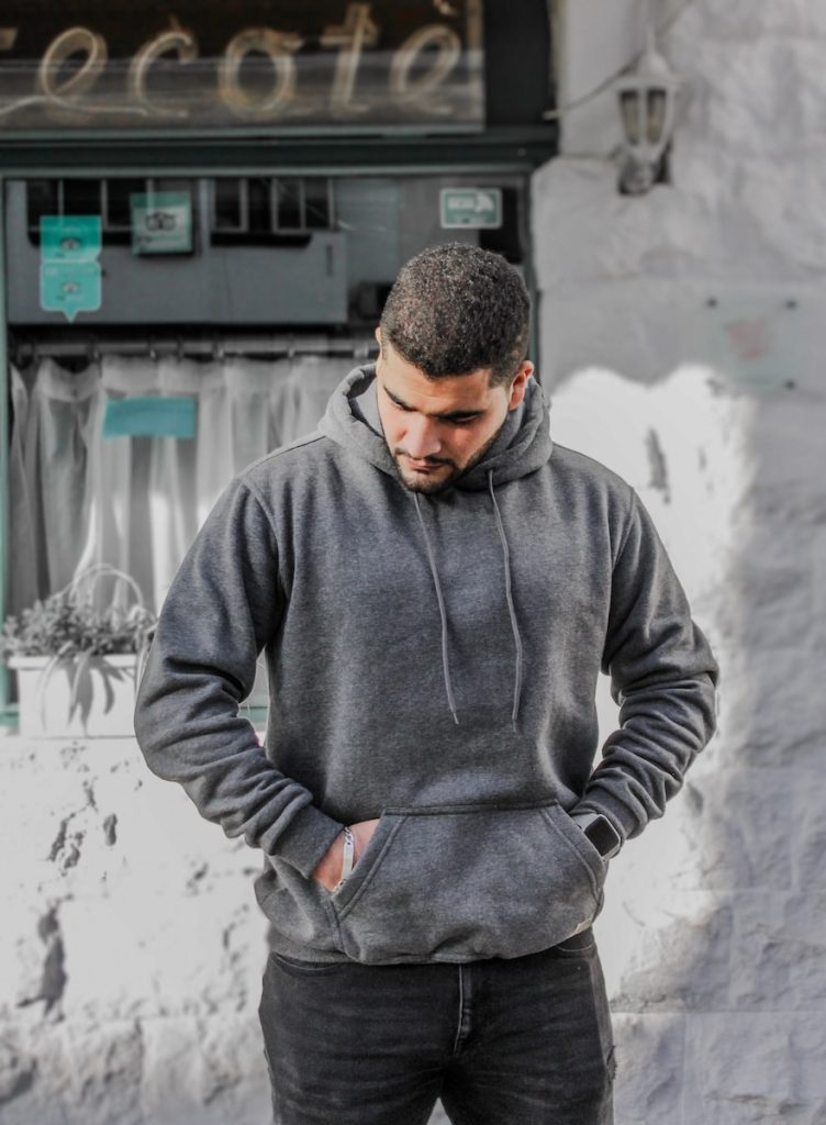 Working out man in gray hoodie standing near white wall