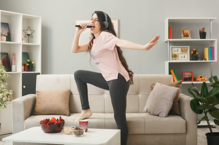 Free Photo Free photo young woman wearing headphones holding microphone sings standing on sofa behind coffee table in living room